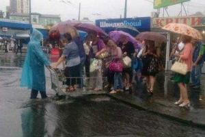 Фото дня: человек в дождевике переправлял киевлянок через дорогу на тележке